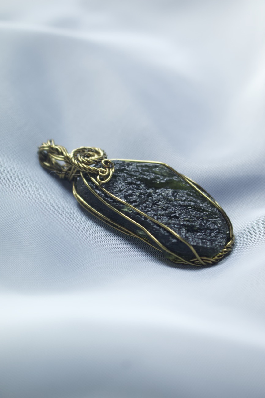 A Moldavite pendant wrapped in gold-coloured wire