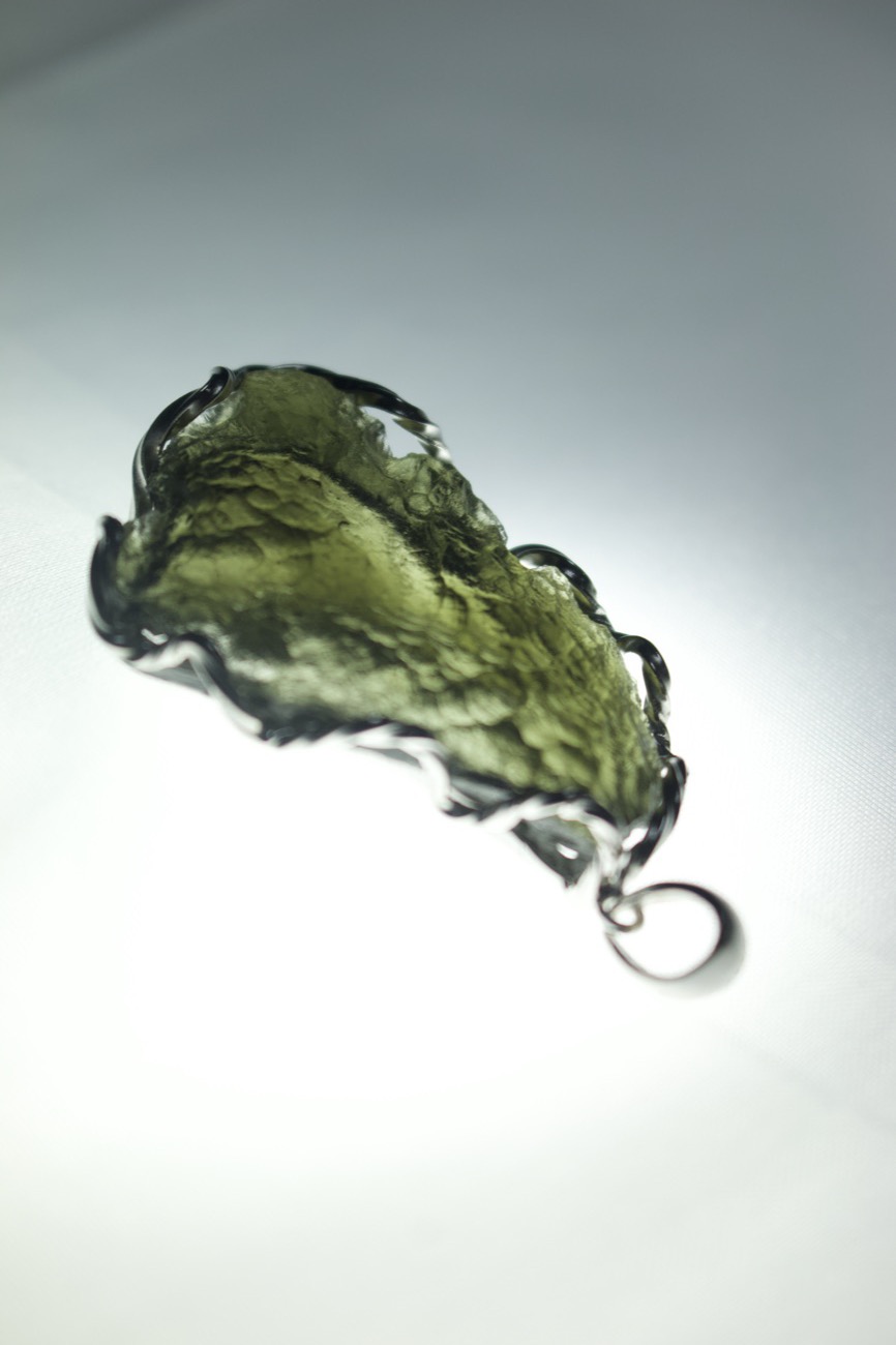 A wire-wrapped Moldavite pendant glowing in the light