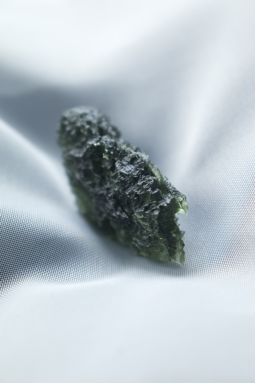 A raw piece of Moldavite with its deeply wrinkled surface, on white silk