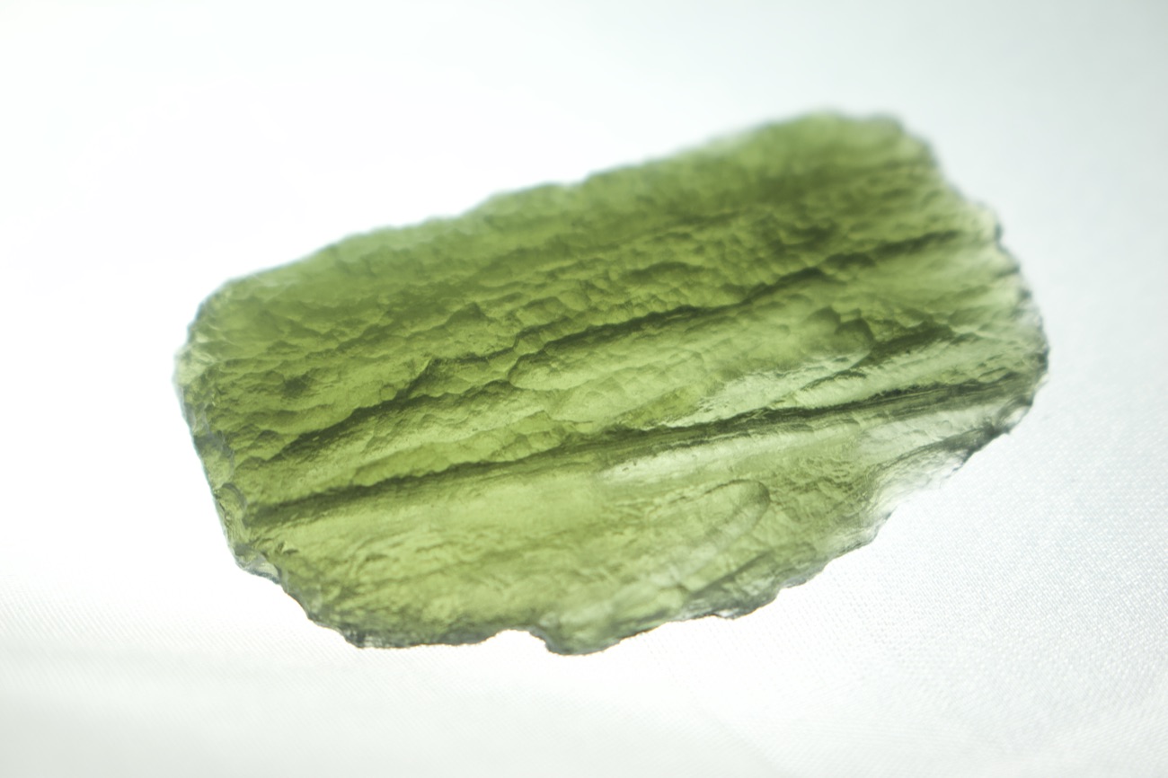 A translucent green piece of Moldavite, lit from behind