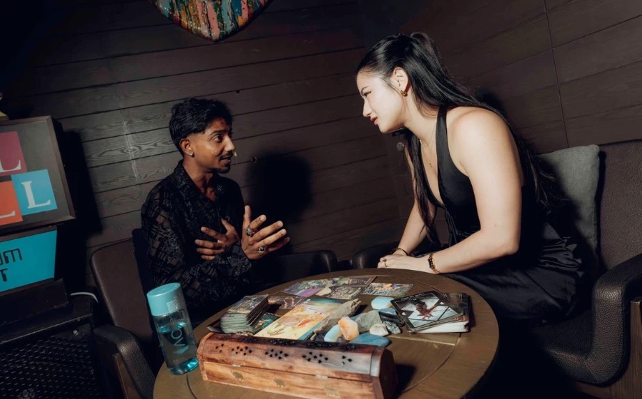 Arvin giving a tarot reading to a guest at an event, cards and crystals spread on a round table